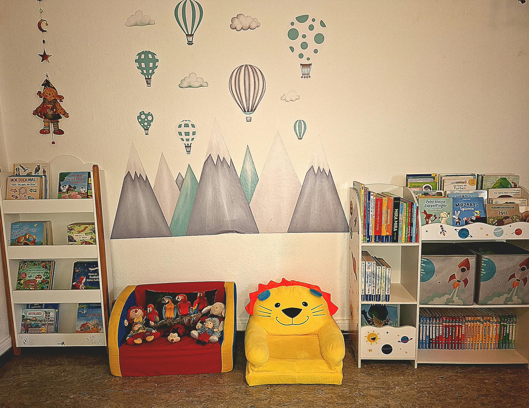 Leseecke mit niedrigen Bücherregalen, einem roten Kindersessel und einem gelben Löwensessel